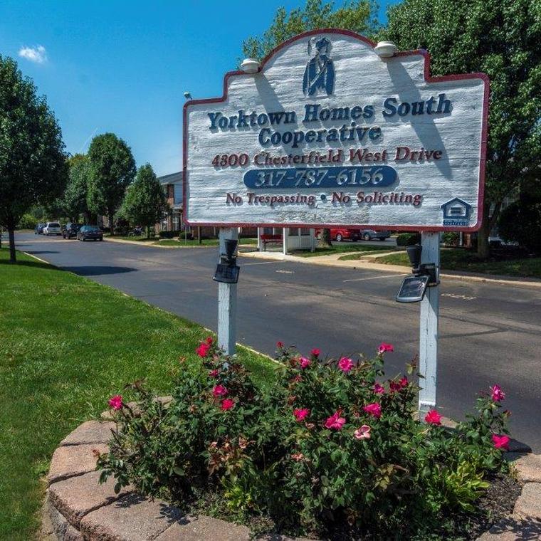 Wooden community sign with stone surrounding and pink flowers at the base