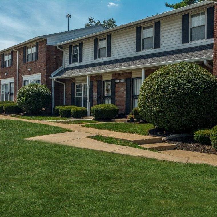 Brick apartment exterior with off white vinyl siding on the upper floor and neatly trimmed green bushes