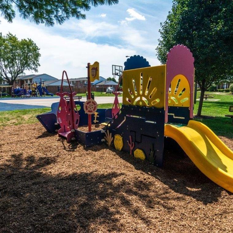 Blue, yellow, and red play gym for smaller children on light brown mulch