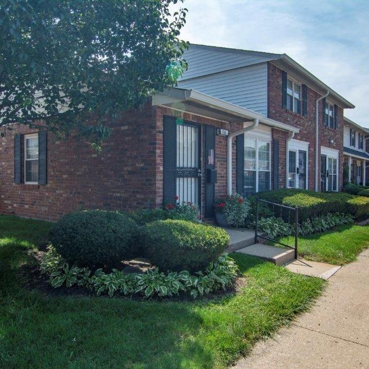 apartment exterior with lush green landscaping and concrete sidewalk