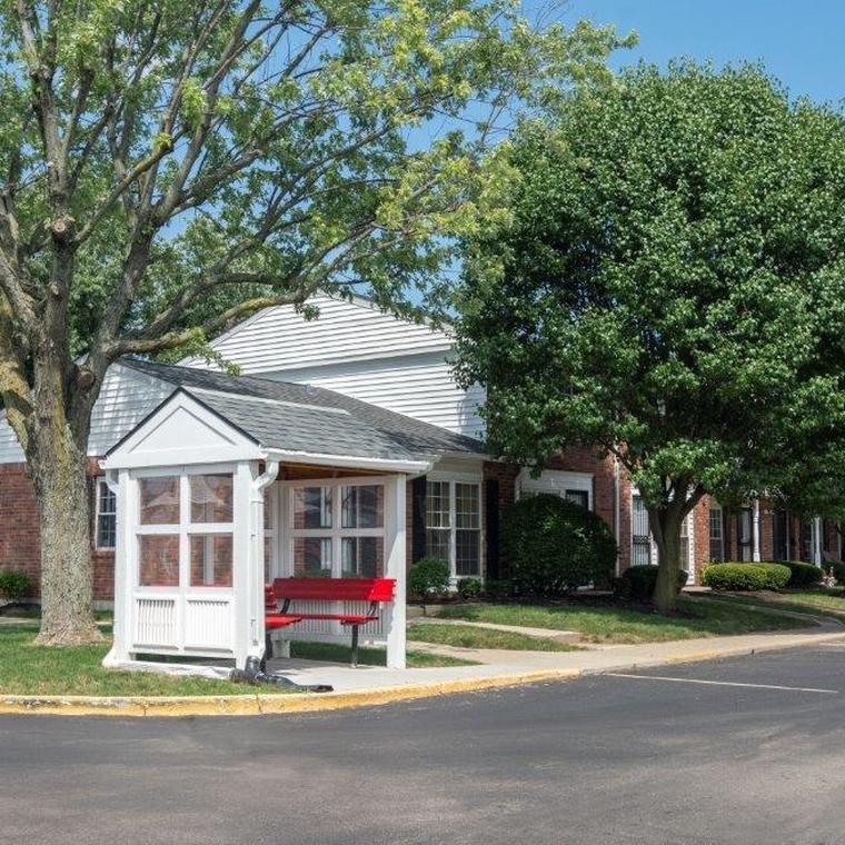 White bus wait station with red benches on curb corner of apartments